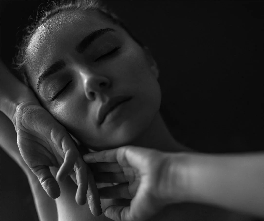 A close-up black and white image of a woman with her eyes closed, resting her head peacefully on her hands.