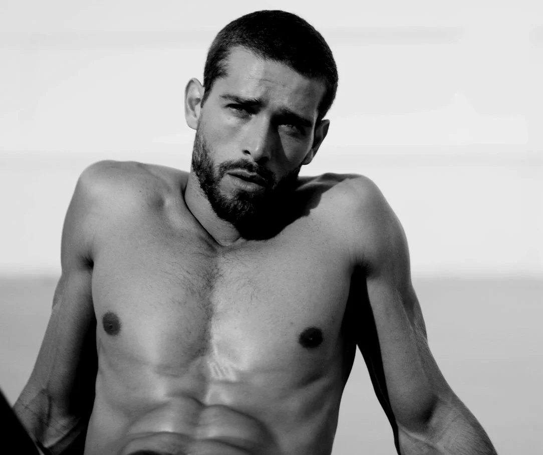 A black and white portrait of a shirtless man with a beard, emphasizing a toned and fit chest.