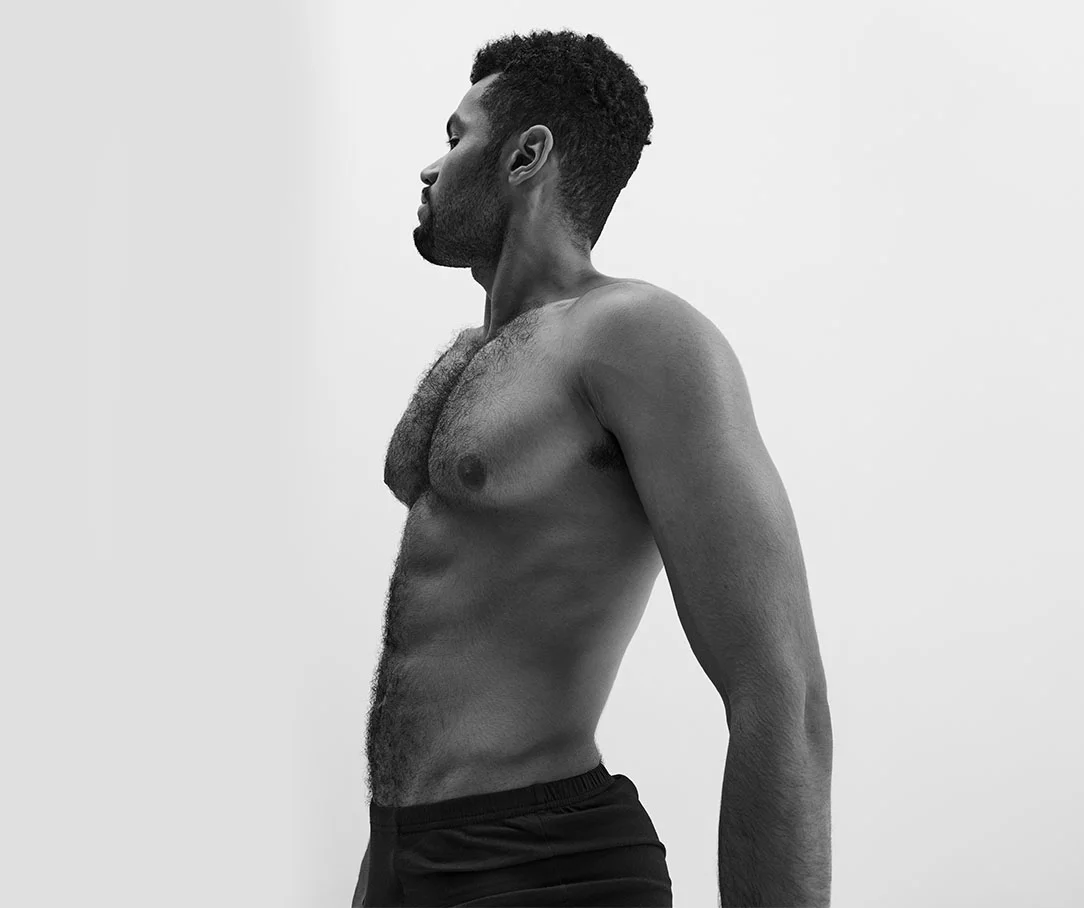 A black and white profile view of a man's torso and lower body, emphasizing his athletic shape.