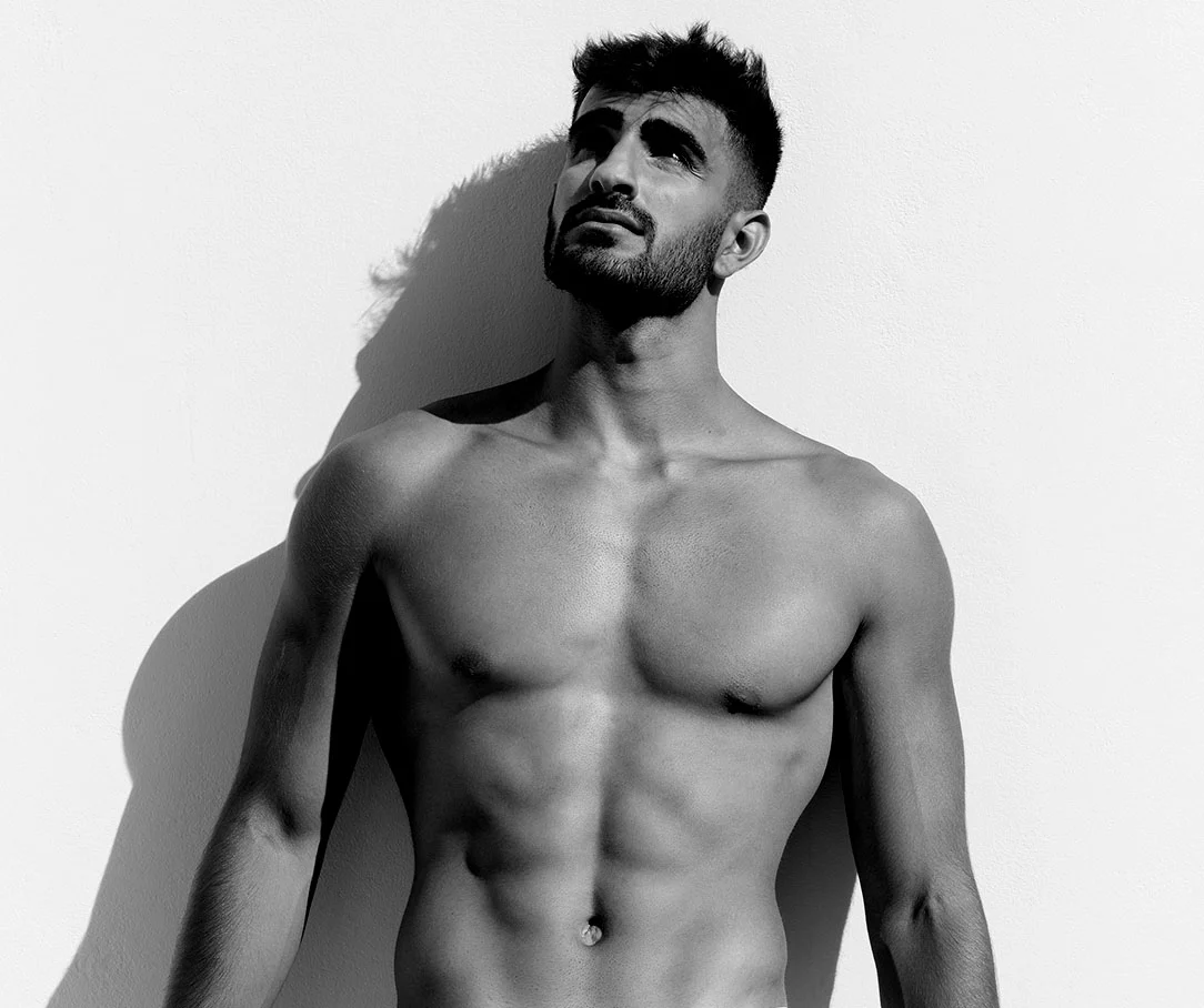 A black and white photo of a muscular man looking upward, showcasing his toned chest and abdominal muscles.