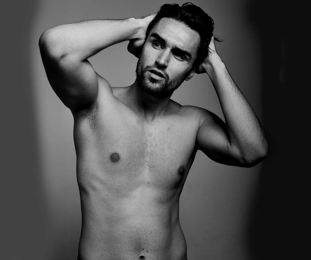 A black and white portrait of a shirtless man with his hands behind his head, showing a fit chest and torso.