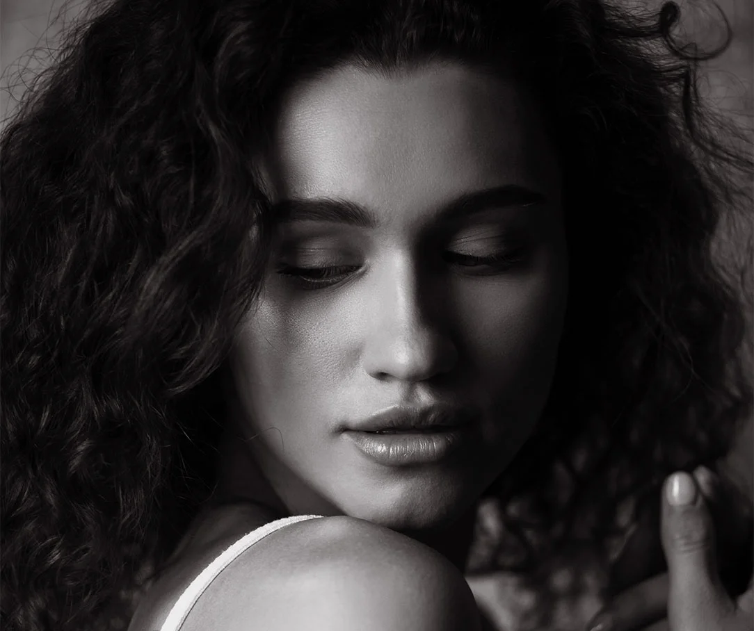 Close-up black and white portrait of a woman with curly hair looking down over her shoulder.